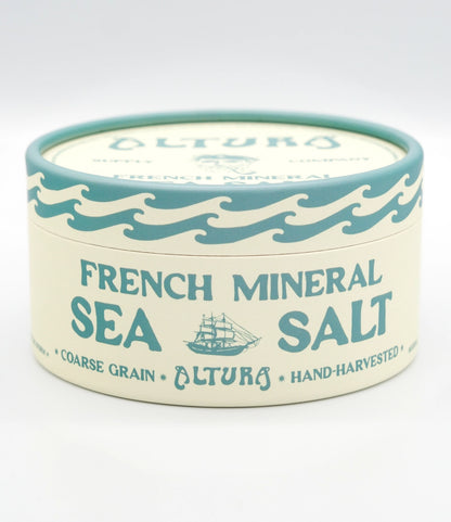 A round tin of Altura French Mineral Sea Salt on a clean white background. The tin has a cream-colored body with teal blue text and wave designs, and a matching teal lid.