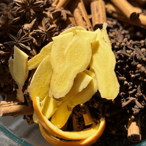 Sliced ginger surrounded by whole cloves, whole star anise, and cinnamon sticks to fresh-press the best elderberry syrup recipe in small batches every month. 