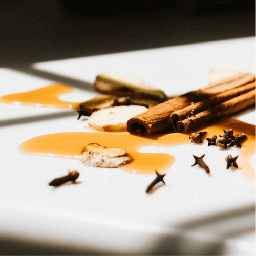 Spilled organic maple syrup on a white countertop, surrounded by a few cloves and cinnamon sticks. Our maple syrup is one of the main sweeteners in our elderberry syrup recipe.