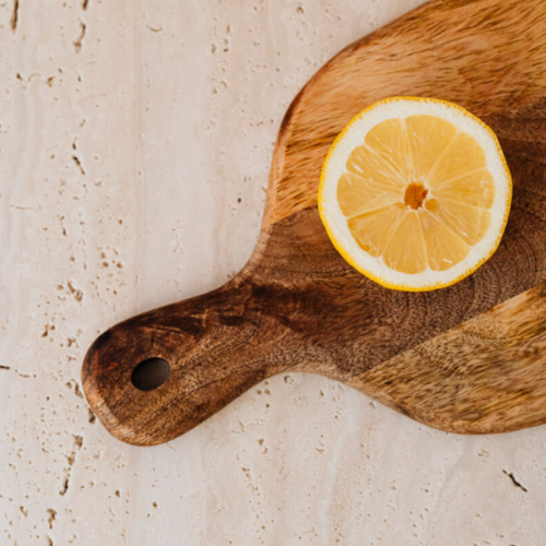 One sliced lemon face up on a wooden cutting board, laying on a white countertop. We infuse lemon into our elderberry syrup recipe for vitamin C's immune-boosting properties.