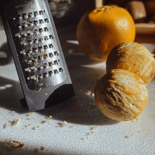 Two grated oranges next to a grater to demonstrate that we hand-grate the orange peels ourselves to make the best elderberry syrup recipe.