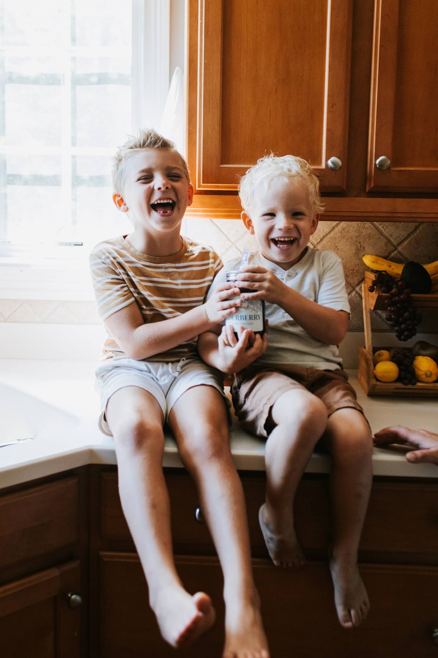 Easton and Nixon, our two boys, sitting on our kitchen counter and laughing while they're holding the best elderberry syrup recipe.