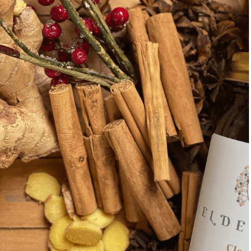 Ceylon cinnamon sticks surrounded by elderberries, ginger, whole star anise, and a jar of the best elderberry syrup.