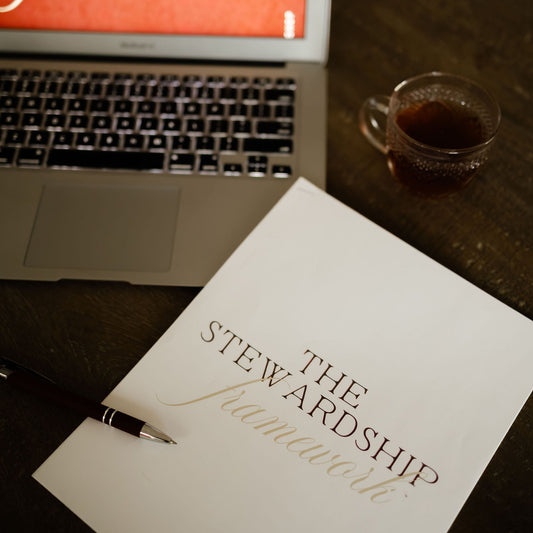 Laptop displaying 'The Stewardship Framework' with a notebook and pen on a table.