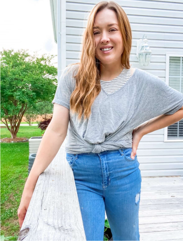 Woman wearing a gray top and blue jeans standing outdoors.