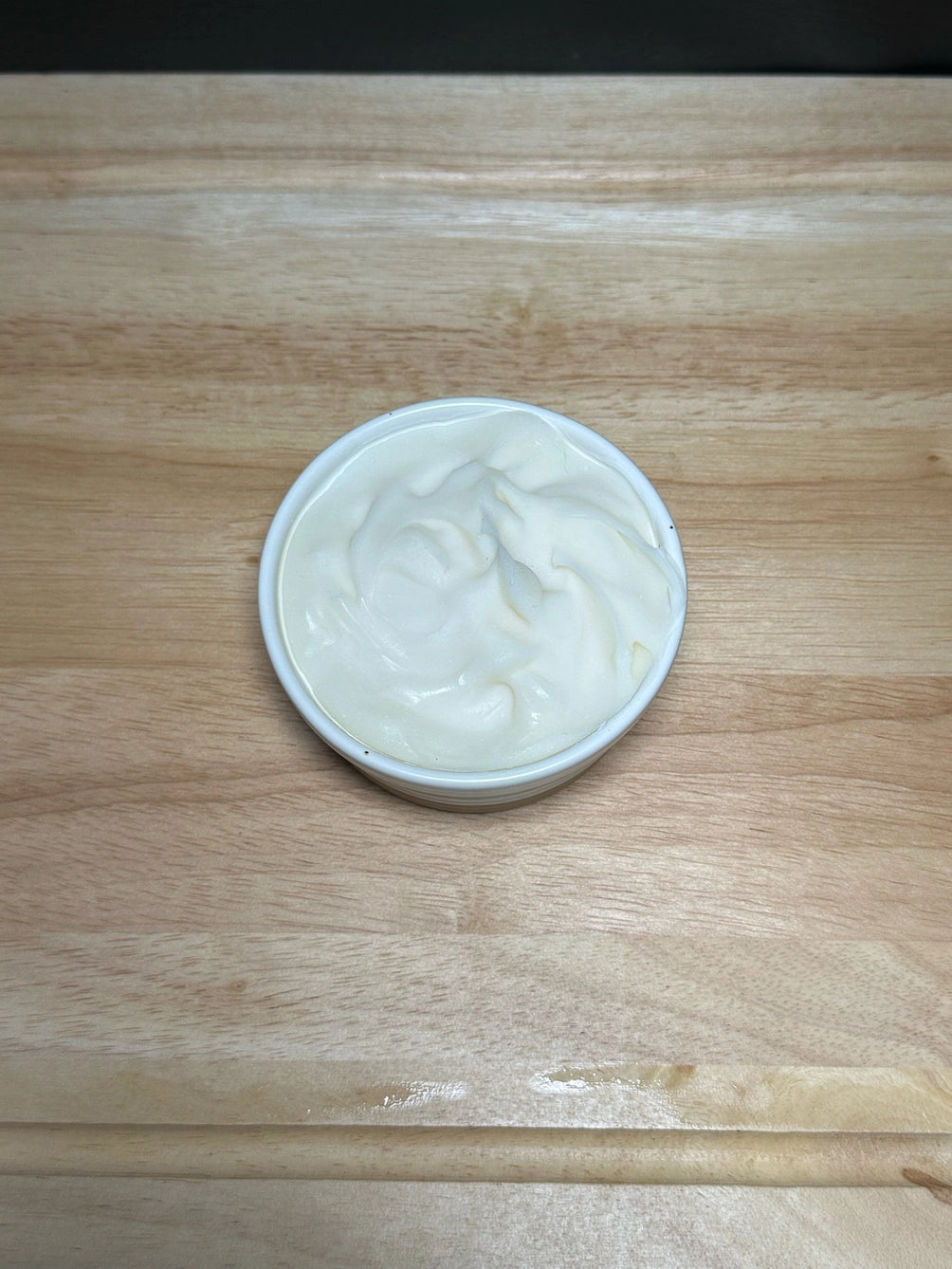 A small white round container filled with tallow dish soap, placed on a light wood surface.