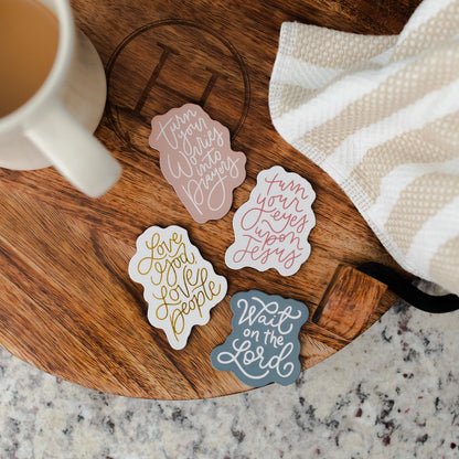 Four Christian inspirational magnets a wooden board with a mug and towel in the background.