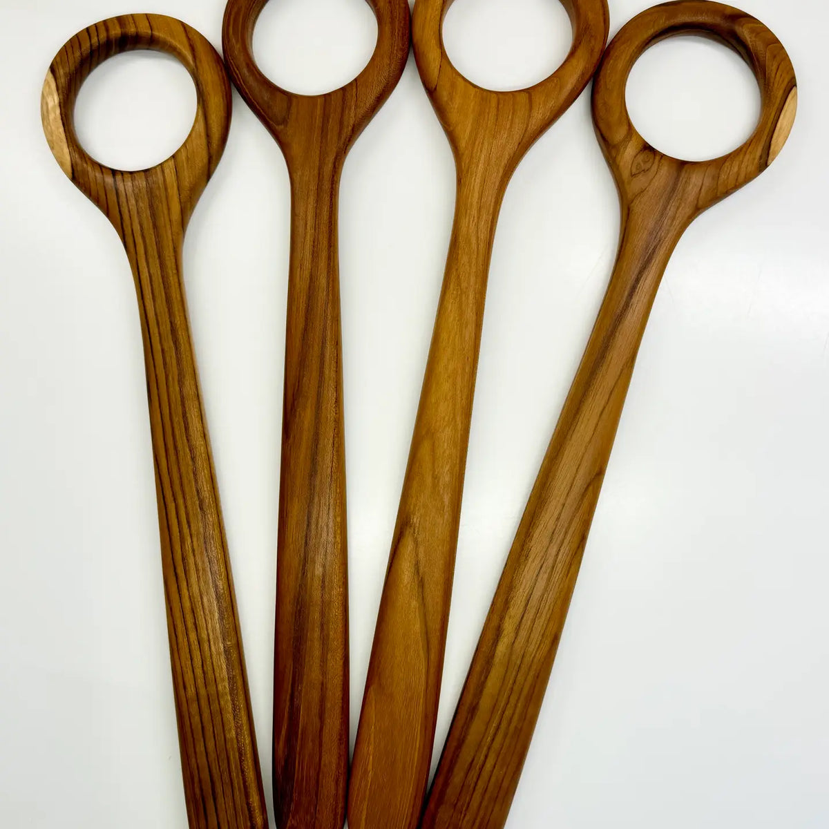 Four wooden spoons with oval loops at the ends, arranged in a fan shape on a plain white background.